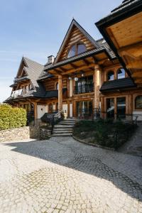 a large wooden house with a stone driveway in front of it at Apartament Skibówki by LoftAffair in Zakopane