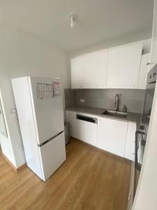 La cuisine est équipée de placards blancs et d'un réfrigérateur blanc. dans l'établissement Appartement JO, proche Paris, à Guyancourt