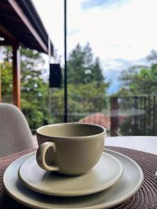 una taza de café sentada en una mesa frente a una ventana en Hospedaria Vila Serra da Luz en Pindamonhangaba