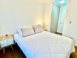 a white bedroom with a large white bed and a table at Departamento Deluxe con Estacionamiento in Los Ángeles