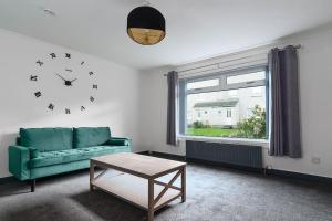 ein Wohnzimmer mit einer grünen Couch und einer Uhr in der Unterkunft Cumbernauld Haven Hideout Sleeps upto 7 in Cumbernauld