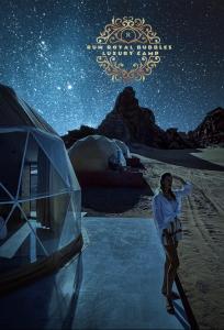 Una donna in piedi accanto a una tenda sotto un cielo stellato di RUM ROYAL BUBBLES lUXURY CAMP a Wadi Rum