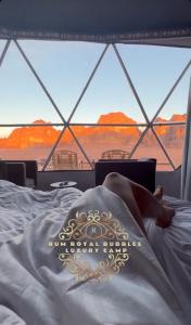 a person laying in bed in front of a window at RUM ROYAL BUBBLES lUXURY CAMP in Wadi Rum