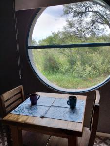 una mesa con dos tazas delante de una ventana en Sankofa Cabañas en Yacanto