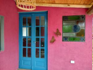 un edificio rosa con una puerta azul y una ventana en Sankofa Cabañas en Yacanto