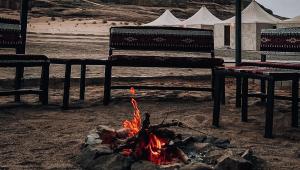 a fire in the sand with two benches and tents at Solana Desert Camp in Wadi Rum