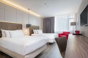 um quarto de hotel com duas camas e uma cadeira vermelha em NH Collection Medellin Royal em Medellín