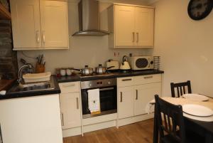 a kitchen with white cabinets and a sink and a table at The Cosy Cottage Retreat! Perfect for Contractors, Relocators, Getaway in Llantrisant +16 photos