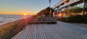 a bench on a sidewalk near the ocean at sunset at Apartament Dar Pomorza 20m do Plaży Ustronie Apartments in Ustronie Morskie