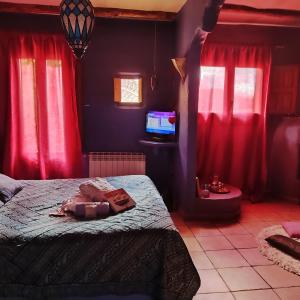 um quarto com cortinas vermelhas, uma cama e uma televisão em El Planeta Escondido em Losana de Pirón