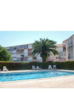 a swimming pool with chairs and a palm tree and a building at LES TERRASSES DE LA BARONNIE Appartement climatisé avec 1 chambre et piscine ouverte du 28 Mai 2025 au 28 Septembre 2025 in Le Grau-du-Roi
