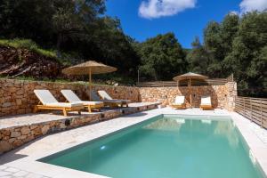a swimming pool with chairs and umbrellas next to a stone wall at Paradise Villas in Sami
