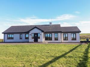 a white house with a black roof on a grass field at 2 Ocean View in Doonbeg