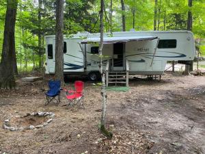 a campsite with two chairs and a caravan in the woods at Betsie -35Ft RV Camper in Woods -Firepit & Hot Tub in Benzonia