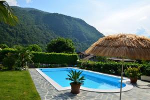 a resort with a swimming pool and a straw umbrella at Großzügiges Ferienhaus mit hohem Komfort auf Gartengrundstück mit Pool fast direkt am See in Colico
