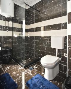 Baño de azulejos negros con aseo y toallas azules en Sobe Zimmer Rooms 2, en Bileća