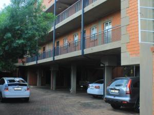 dois carros estacionados num parque de estacionamento em frente a um edifício em Lea's Furnished Apartments - Lofts at Loftus em Pretoria