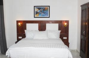 Schlafzimmer mit einem weißen Bett mit einem Kopfteil aus Holz in der Unterkunft Hotel BKBG Benin in Cotonou