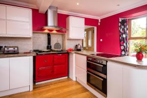 a red kitchen with white cabinets and a red oven at Schönes Ferienhaus in Blairgowrie mit Grill, Terrasse und Garten in Blairgowrie