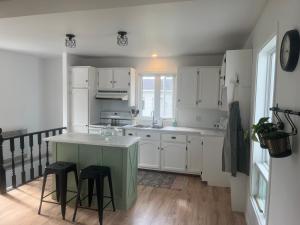 una cocina con armarios blancos y una isla con taburetes en Gite - La ruée vers l'orge, en Trois-Rivières