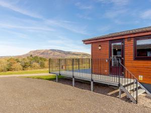 a wooden cabin with a balcony with a mountain in the background at 2 Bed in Loch Leven 82297 in Kinross