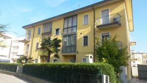 un bâtiment jaune avec une clôture devant lui dans l'établissement Große Wohnung in Rosolina Mare mit Grill und Garten, à Rosolina Mare