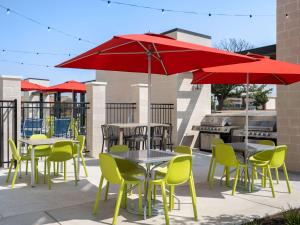 eine Terrasse mit Tischen, Stühlen und roten Sonnenschirmen in der Unterkunft Home2 Suites By Hilton Round Rock Medical Center in Round Rock