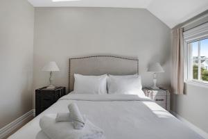 a white bedroom with a large white bed with a chair at Grande Vista 5Br Manor with Pool & Mt Eden Views in Auckland