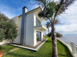 een wit huis met een palmboom en de oceaan bij The best sea view in Madeira - Casa Farol in Fajã da Ovelha