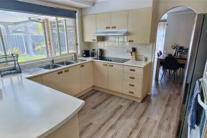 a kitchen with white cabinets and a dining room with a table at Twin Palms @ The Basin in St Georges Basin