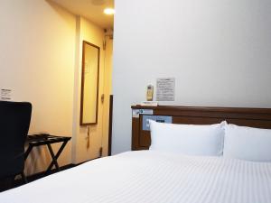 a bedroom with a bed with white sheets and a chair at Hotel Route-Inn Tsuruga Ekimae in Tsuruga