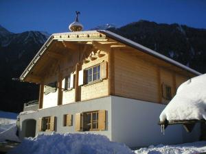 un edificio cubierto de nieve con montañas de fondo en Ferienhaus in Sautens mit Garten, Pool und Grill und Panoramablick en Sautens