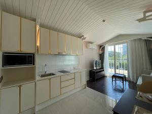 a kitchen with white cabinets and a living room at Grand Florida芭提雅私家海滩花园公寓E206 in Na Jomtien