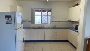a kitchen with white cabinets and a white refrigerator at Lowset home with attached Granny Flat - Doomba Dr, Bongaree in Bongaree