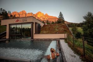 Una donna seduta in una piscina di fronte a una casa di Moseralm Dolomiti Spa Resort a Nova Levante