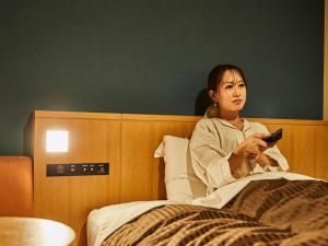 a woman sitting in bed holding a remote control at Kansai Airport Washington Hotel in Izumi-Sano
