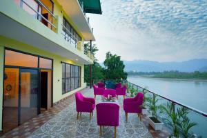 - un balcon avec des chaises roses, une table et de l'eau dans l'établissement The Neeraj Naturecure On Ganga, à Rishikesh