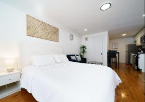 a white bedroom with a white bed and a kitchen at Comfy Studio in UES! Perfect for 2! in New York
