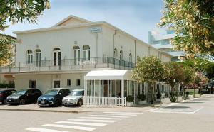 un edificio blanco con coches estacionados frente a él en Hotel Ginevra en Lido di Jesolo