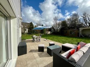 une terrasse avec un canapé, des tables et un parasol dans l'établissement Maison chaleureuse, décoration raffinée, à Clohars-Fouesnant