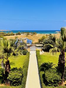 a walkway through a park with palm trees and the ocean at Karteros Hotel in Karteros