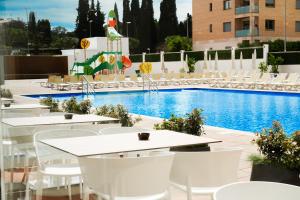 a pool with white tables and chairs in front of a hotel at htop Amatista #htopBliss in Lloret de Mar