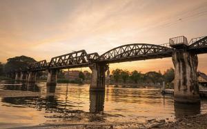 a train bridge over a river with the sun setting at Noot's Bar And Guesthouse in Kanchanaburi
