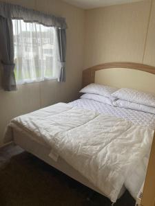 a bedroom with a bed with white sheets and a window at 8 Berth Caravan At The Seaside Of Haven Hopton-on-sea In Norfolk Ref 80065f in Great Yarmouth