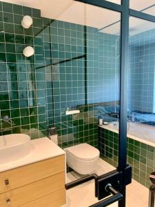La salle de bains est pourvue de carrelage vert, de toilettes et d'un lavabo. dans l'établissement New appartment with art collection, à Vilnius