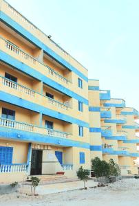 a large building with blue balconies and trees in front of it at Anglo Chalets - Ageeba beach in Marsa Matruh