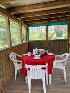 una mesa con sillas blancas y un mantel rojo en el porche en Mobilhome, en Castillonnès