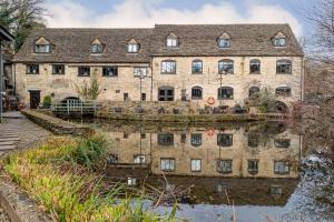 an old stone building with a reflection in the water at Egypt Mill Hotel and Restaurant in Nailsworth