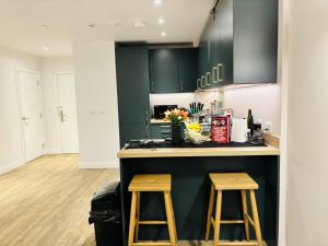 una cocina con armarios verdes y una barra con 2 taburetes en Your London Escape Luxurious 1 Bedroom Apartment, en Londres