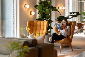 a woman sitting in a chair reading a book at Comfort Hotel Park in Trondheim